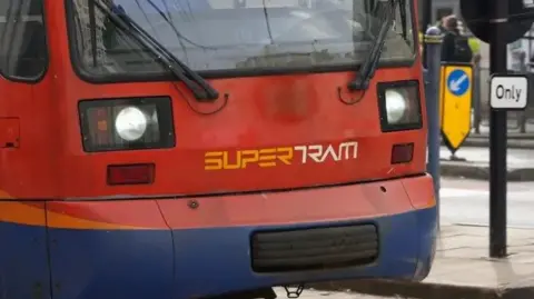 A red tram makes its way down a city street. The word 'Supertram' is emblazoned across the front