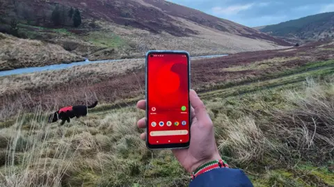 Vodafone is a man in the middle of a mountain in West Wales, there is a place of your green and blue sky, with a river and a dog. 