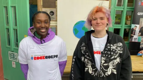 Ujanah and Nellie are smiling at the camera. They are both wearing white t-shirts.