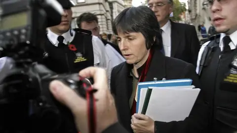 Getty Images A younger looking Cressida Dick outside the Old Bailey in London flanked by police officers in 2007. She is carrying a pile of papers and a photographer is in the foreground taking a photo of her. 