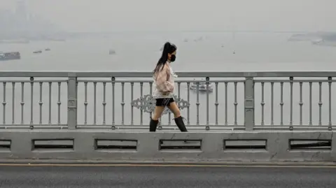 Getty Images Seorang wanita berjalan di jembatan Wuhan di atas sungai Yangtze di Wuhan, di provinsi Hubei tengah, Tiongkok pada 22 Desember 2024