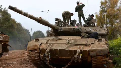 Israeli soldiers stand on top of a tank in northern Israel, near the Israel-Lebanon border. the tank is an imposing presence, taking up most of the frame.