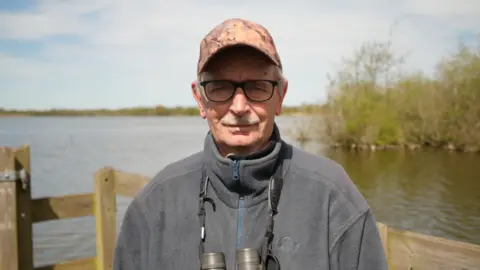 Shaun Whitmore/BBC Brian Smith, a man standing at NWT Ranworth wearing a zip up grey fleece