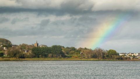 Cloudy skies over a lake with a small rainbow emerging 