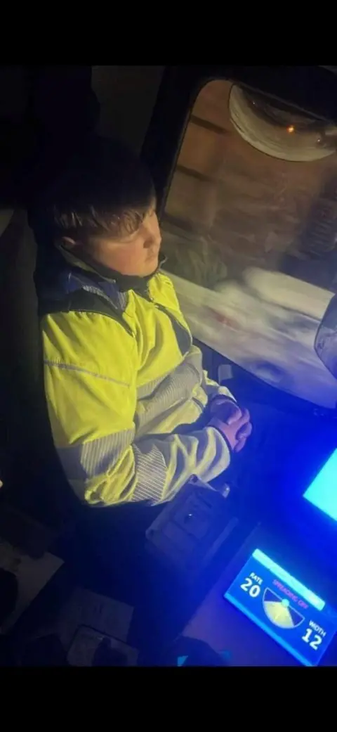 Jamie wearing a yellow jacket is asleep in the cab of a lorry