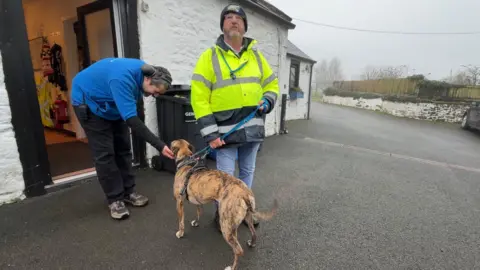A man in a high-vis jacket walks a dog