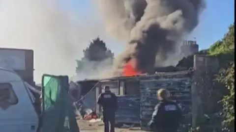 Flames and smoke coming from above one of the garages. There are two officers heading towards the flames and smoke.