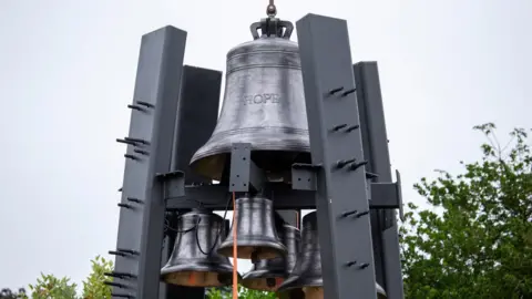 A big bell with HOPE cast on it held up by four steel supports