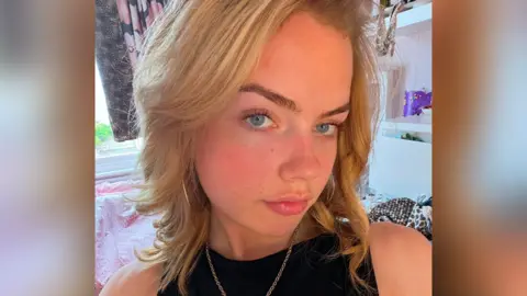 Luisa Spence Luisa Spence. She has long blonde hair and blue eyes. She is wearing a black top and a gold necklace. Her face is turned slightly from the camera