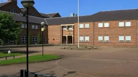 Google A pale-brick two-storey building with lots of windows and a bricked forecourt 