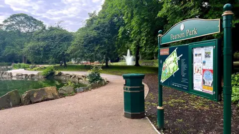 View of Pearson Park with a large green sign and map in the foreground and a pound and fountain in the background