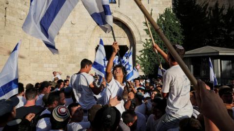 Young Israelis wave flags outside the entrance to the Muslim quarter of Jerusalem's Old City, in occupied East Jerusalem,at the start of the Jerusalem Day flag march (5 June 2024)