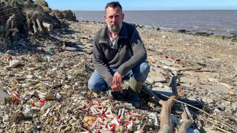 Yvette Austin/BBC Fossil hunter Daniel Hogburn with a small sample of vials he's found 