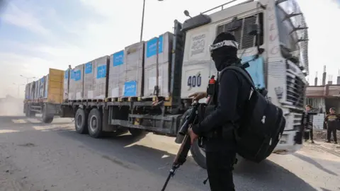 Getty Images Truk bantuan kemanusiaan memasuki Rafah ketika seorang pria berpakaian hitam bersenjatakan senapan berdiri mengawasi