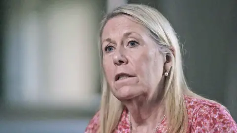 Head and shoulders changeable  of Dr Sandie Bohin - with consecutive  blond hairsbreadth  and a pinkish  and reddish  patterned top.  