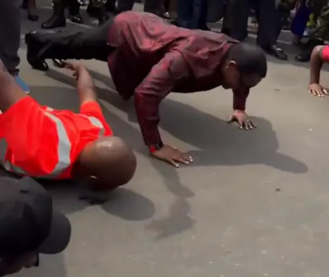 Lazarus Chakwera/Facebook Lazarus Chakwera wearing a red shirt and black trousers doing push-ups in the street.