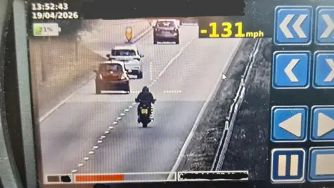 Norfolk and Suffolk Speed Cameras An image of a speed camera monitor showing a motorcyclist riding in the right hand lane on the A14. There are cars in the left-hand lane. At the top in bright yellow is the speed he is travelling - 131mph - and on the right of the screen are blue buttons.