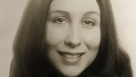 Family Handout Black and white headshot of a woman with long hair smiling at the camera.