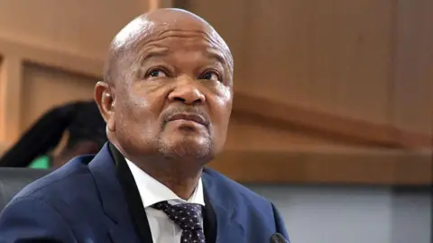 Gallo Images via Getty Images Foto da cabeça e ombros de Senzo Mchunu vestindo paletó azul e gravata. Ele está olhando para a direita.