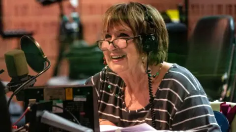 Dame Jenni Murray smiling at the microphone in a BBC radio studio in 2020