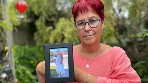 Woman in a salmon pink shirt holding up a picture frame with a woman pictured wearing a long white flowy dress