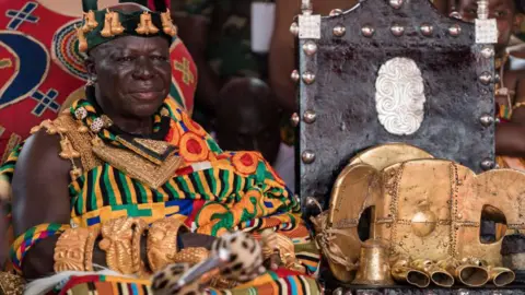 King Otumfuo Osei Tutu II in ceremonial dress and wearing a gold crown and jewellery