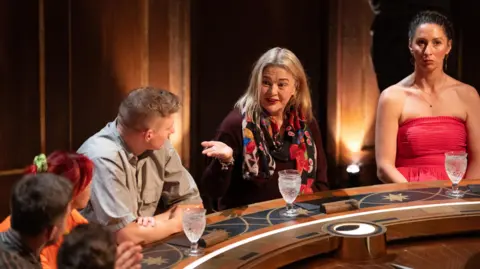 BBC/Studio Lambert/Euan Cherry Harriet Tyce - second from the right - with blonde hair, sitting at a roundtable discussion during filming of the Traitors.
