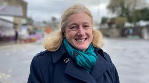 Woman with shoulder-length blonde hair and a blue coat