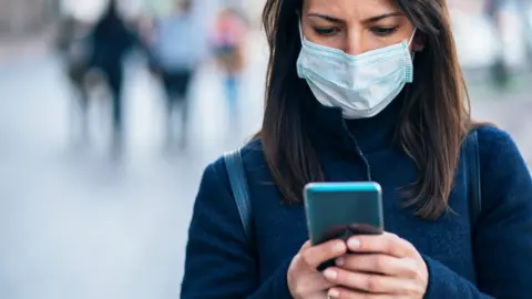 Getty Images woman wearing face mask, holding phone