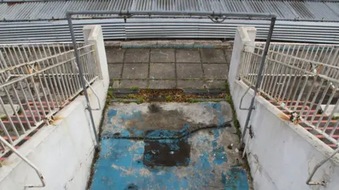 Deborah Norwood This is the old ladies rinse-shower as you come out of the changing rooms to the pool side, looking down from the stairs of the viewing terrace above.