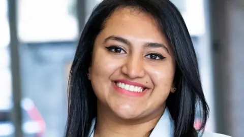 Rhea Thomas, a young woman with dark hair smiling for the camera