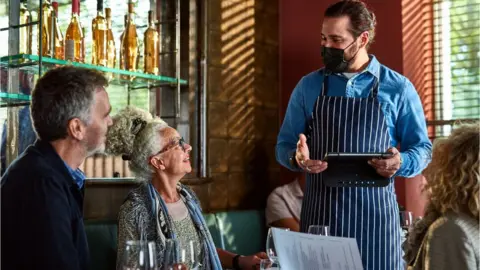 Getty/10'000 Hours Man wearing face mask handing menu to woman, dining out, the new normal, weekend activities, food and drink