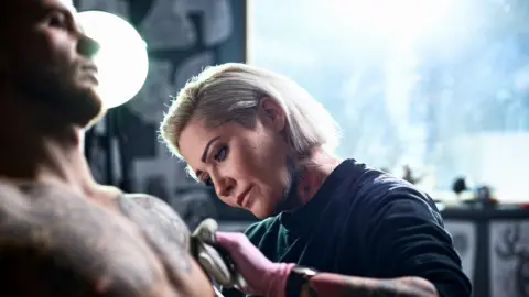 Getty Images Female tattoo artist working on a male client