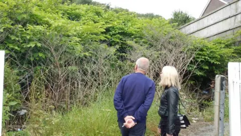 Robin Waistell showing Eye on Wales presenter Nellie Bird the Japanese knotweed next to his property