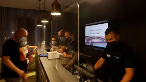 Reuters German tourists are attended by receptionists, wearing protective face mask as they do the check-in at the Catalonia Ronda hotel, in southern Spain