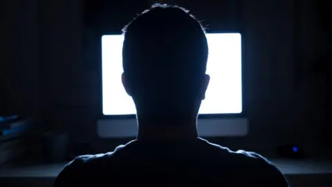 Getty Images Silhouette of man's head in front of computer monitor light at night