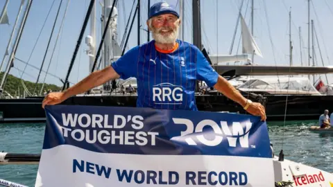 World's Toughest Row Frank Rothwell on a boat with 'world record' banner after his Atlantic row