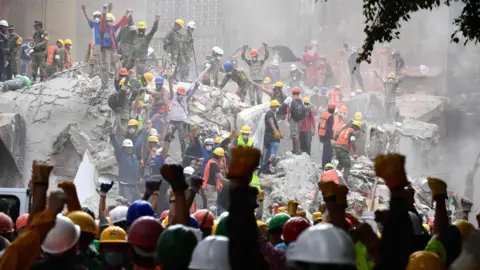 AFP Rescuers raise their fists for silence at the site of a collapsed building in Mexico City