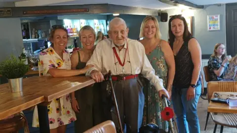 BBC Alan standing in a pub with four female relatives