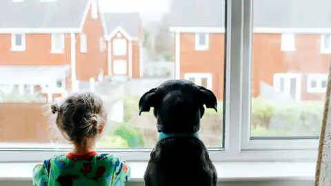 Getty Images Little girl looks out window to empty street