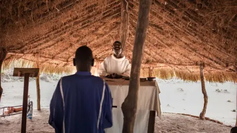 AFP A man and a priest in Southern Sudan stood inside a hut at the refugee camp of Obo The man has his back turned facing the priest as he conducts mass.