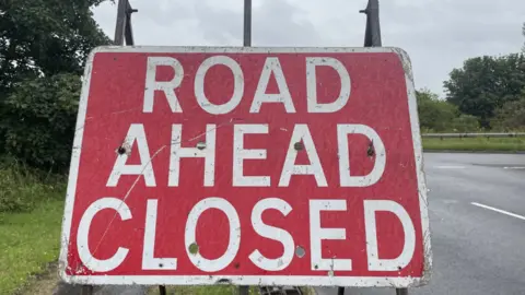 A close-up photo of a red 'Road Ahead Closed' sign.