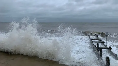 BBC Waves crash over the coast road at Walcott, Norfolk