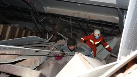 EPA A rescuer follows an injured man walking out of the rubbles of a collapsed five-story hotel building in Quanzhou city in southeast China's Fujian province, 7 March 2020