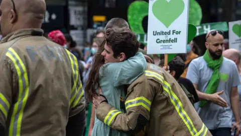 Getty Images Fireman hugs a woman at a Grenfell memorial event