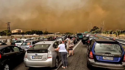 Getty Images Cars are blocked at the closed National Road during a wildfire in Kineta, near Athens