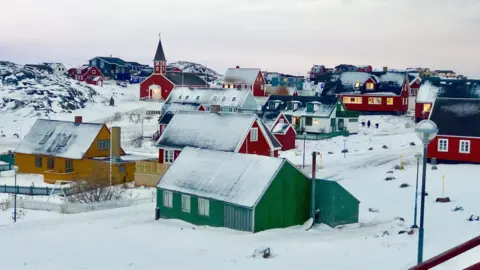 BBC A town in typical Greenland style is pictured - brightly-painted wooden walls and triangular roofs covered in snow are the main features of these sparsely dotted homes