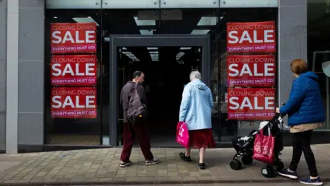 Getty Images People enter a shop advertising a closing down sale in Leeds, United Kingdom.