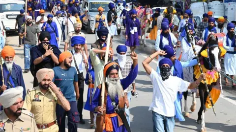 Getty Images Supporters of Quami Insaaf Morcha protest march, on March 19, 2023 in Mohali, India. Hundreds of Sikh protesters, under the banner of Qaumi Insaaf Morcha, laid siege to Gurdwara Singh Shaheedan Chowk in Sohana soon after reports of Punjab Police detaining Waris Punjab De chief Amritpal Singh and his supporters started making rounds on Saturday.