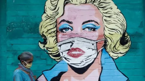 A woman wearing a protective mask walks past a graffiti depicting former American actress Marilyn Monroe wearing a mask, amidst the spread of the coronavirus disease (COVID-19), on a street in Mumbai, India, March 30, 2021.